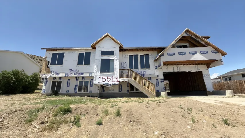 New construction residence with an attached garage, multiple windows, a prominent wooden staircase, and an undeveloped lot
