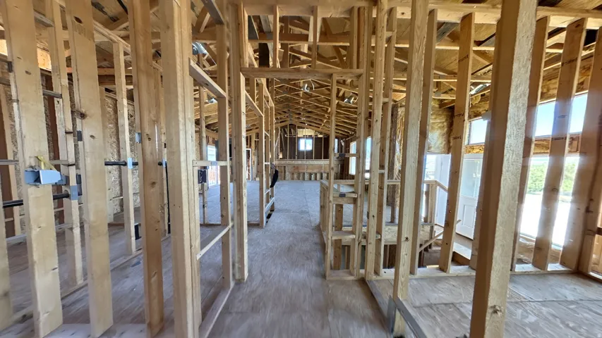 Interior framing showcasing a plywood subfloor, exposed wooden studs, and visible ceiling joists