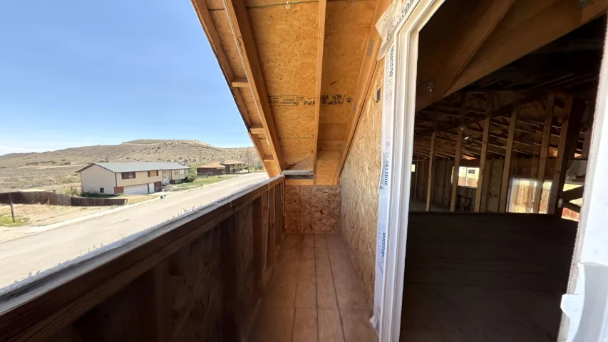 Unfinished interior space with exposed wood framing, an open doorway, and a partially enclosed outdoor area