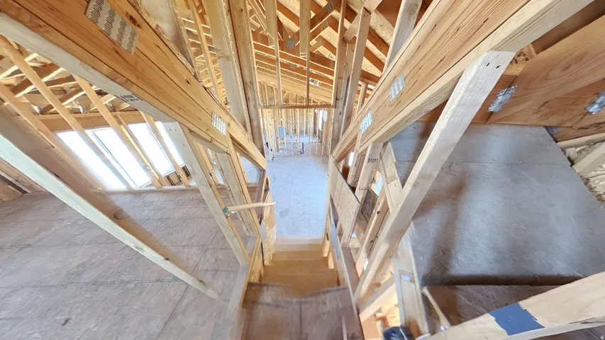 Unfinished interior framing showcasing exposed wood beams, subflooring, and a developing staircase