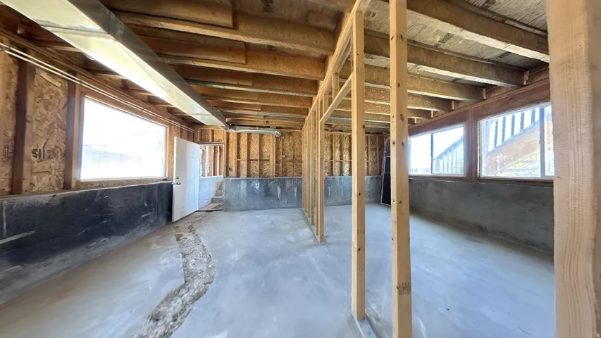 Unfinished basement space featuring exposed wooden ceiling joists, concrete flooring, and multiple windows