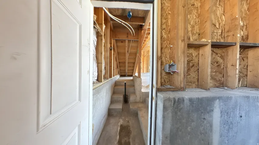 Unfinished basement featuring exposed wood framing, poured concrete walls, and concrete stairs