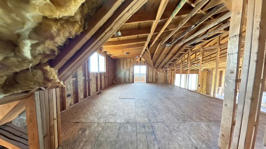 Expansive unfinished attic space featuring exposed wood framing, plywood subflooring, multiple window openings, and visible insulation
