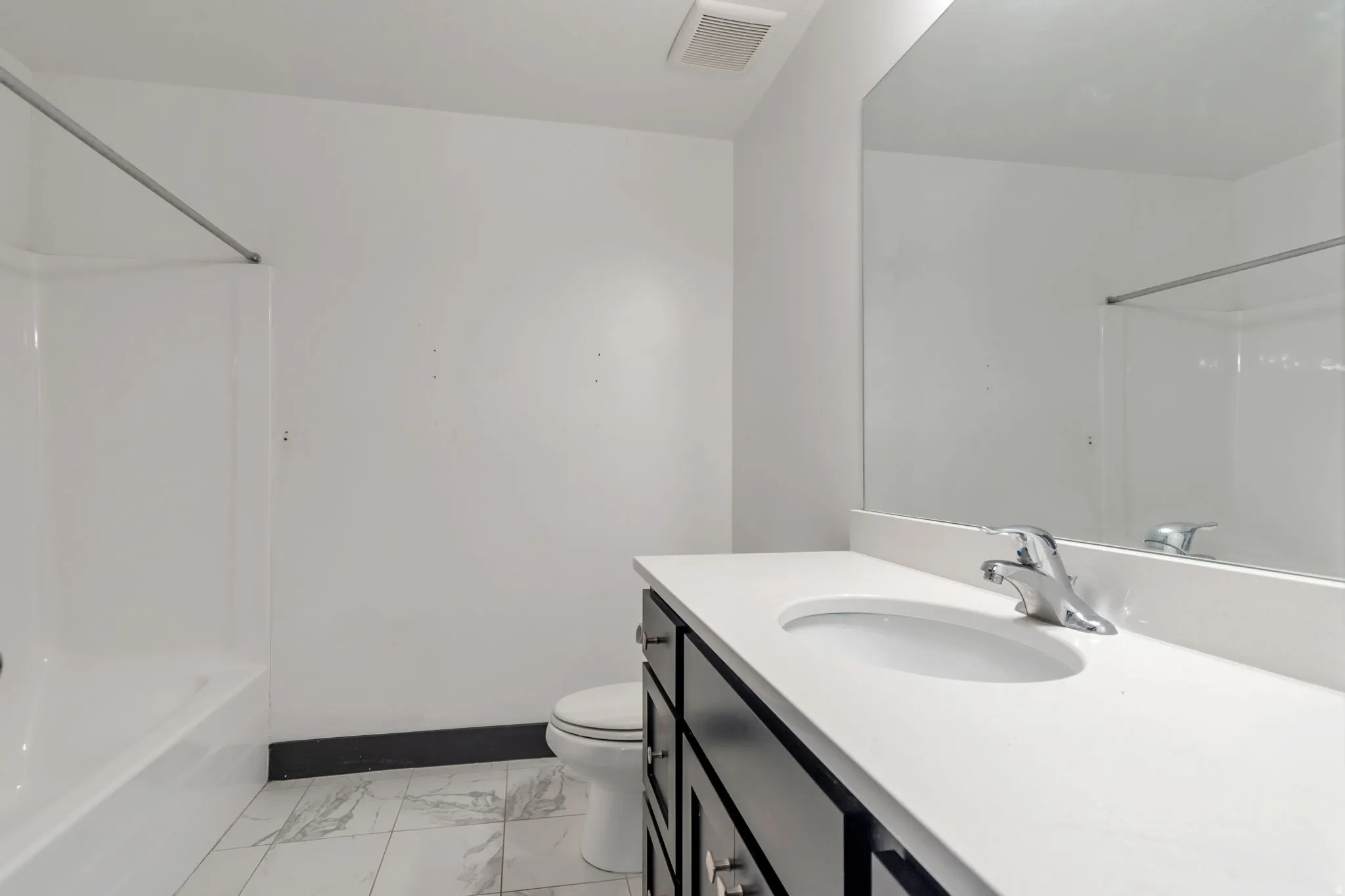 Bathroom featuring a white bathtub, a toilet, a vanity with a white countertop, a basin sink, and a mirrored wall