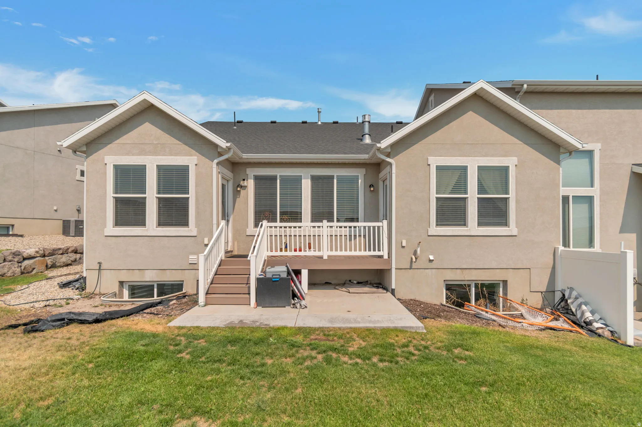 Rear exterior featuring a deck with white railings, a ground-level concrete patio, and a manicured lawn