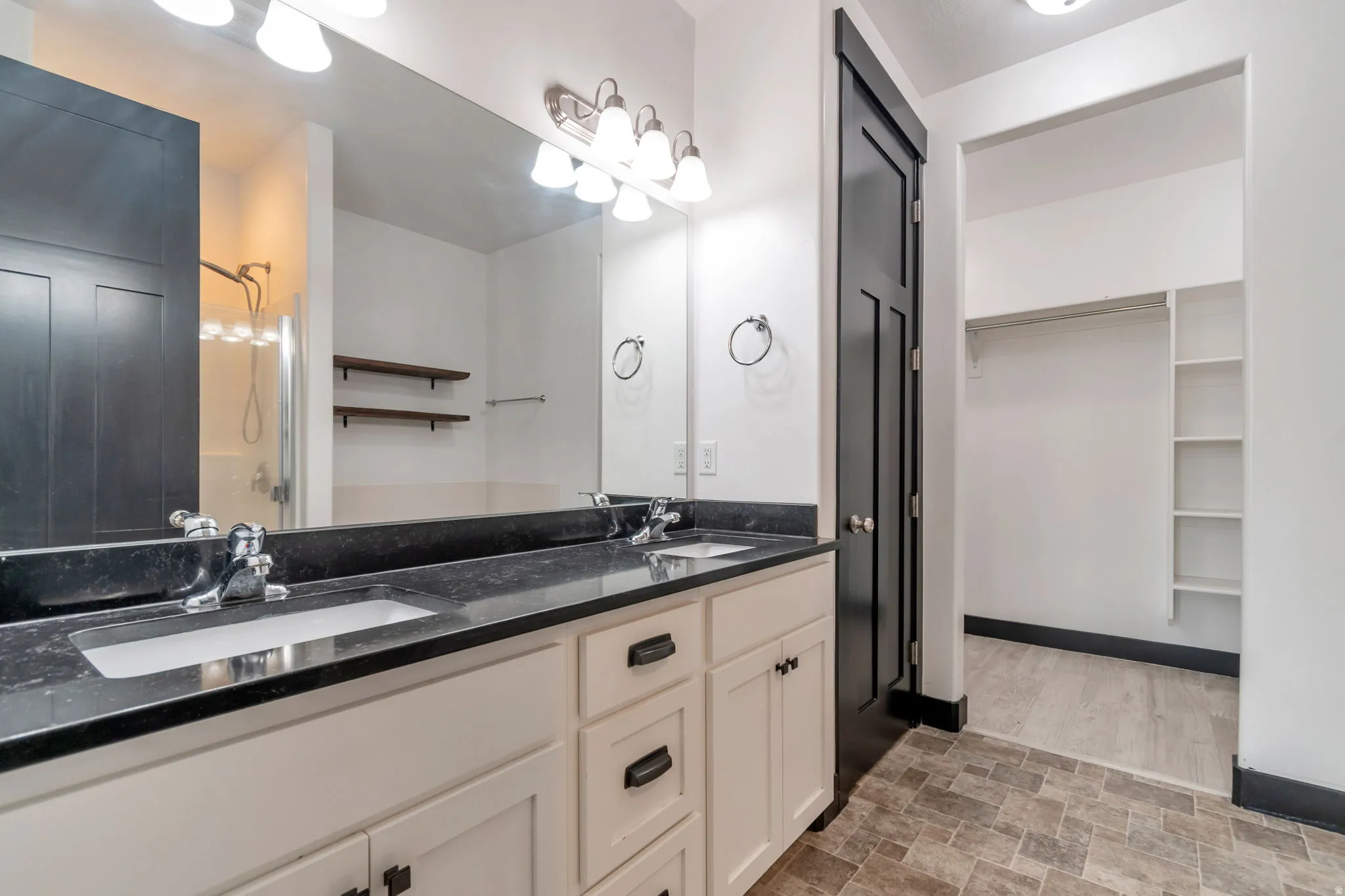 Double vanity with a dark countertop and white cabinetry, brushed nickel faucets, and coordinating overhead lighting