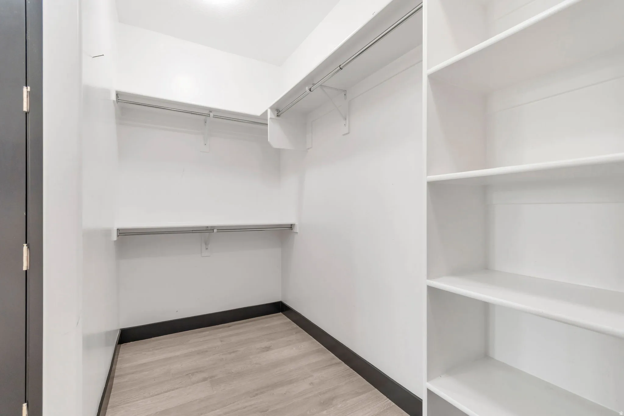 Walk-in closet featuring light wood-finish flooring, white walls, dark baseboards, built-in shelving, and hanging rods