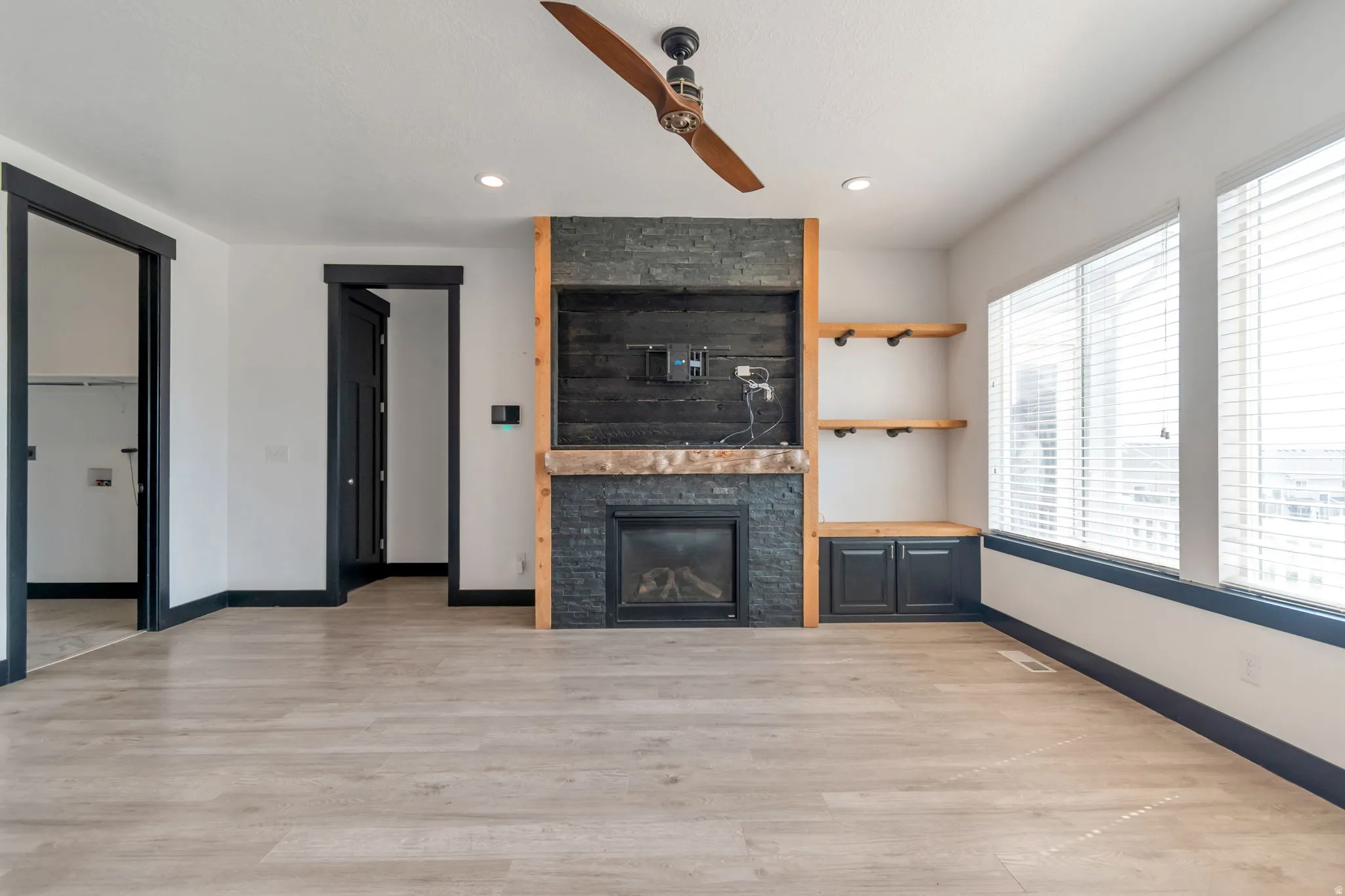 Living space featuring a stone-clad fireplace with a wood mantle, custom built-in shelving, and light wood-finish flooring