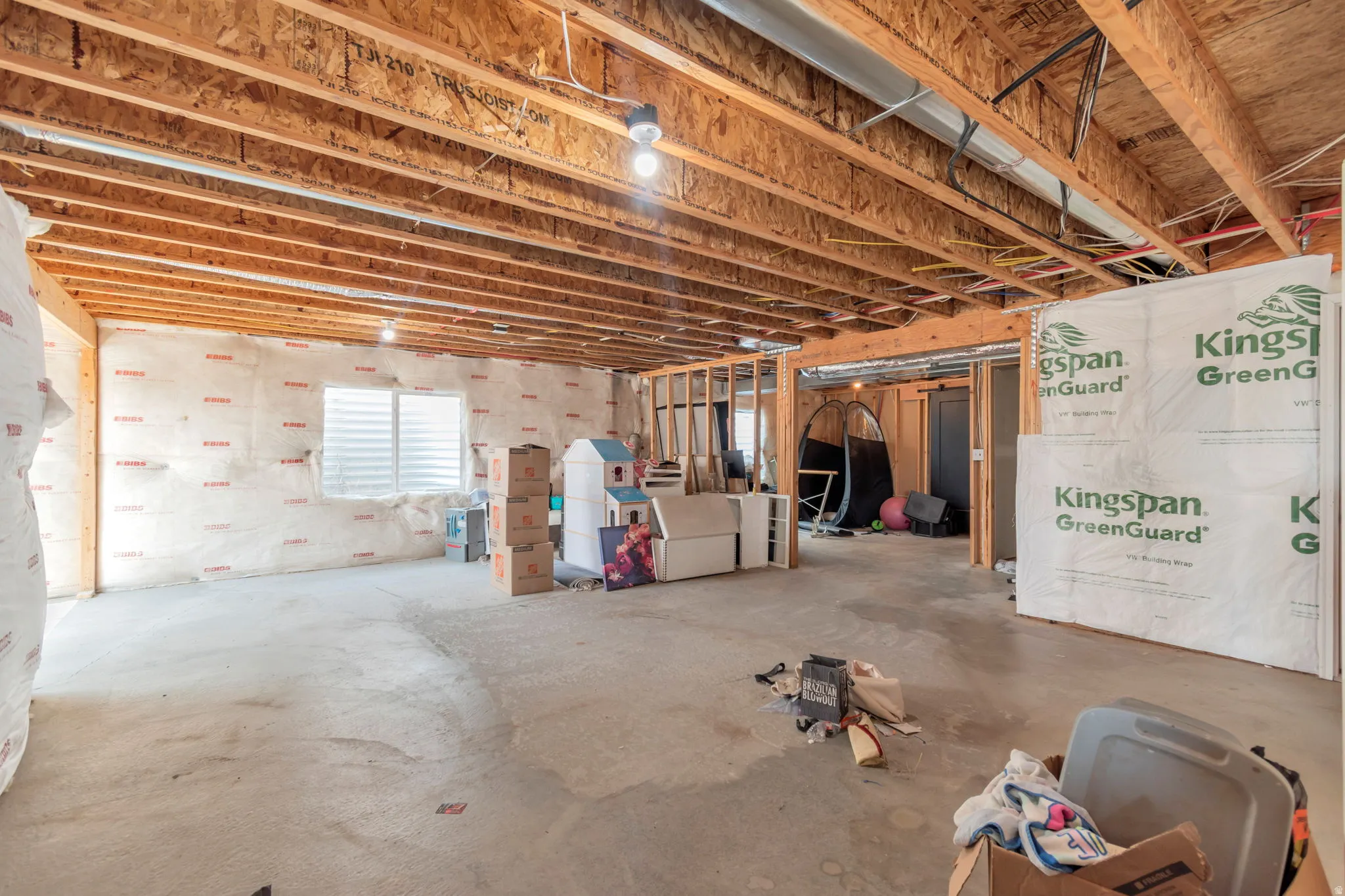 Unfinished basement featuring exposed wood joists and subflooring, concrete slab flooring, and a single egress window