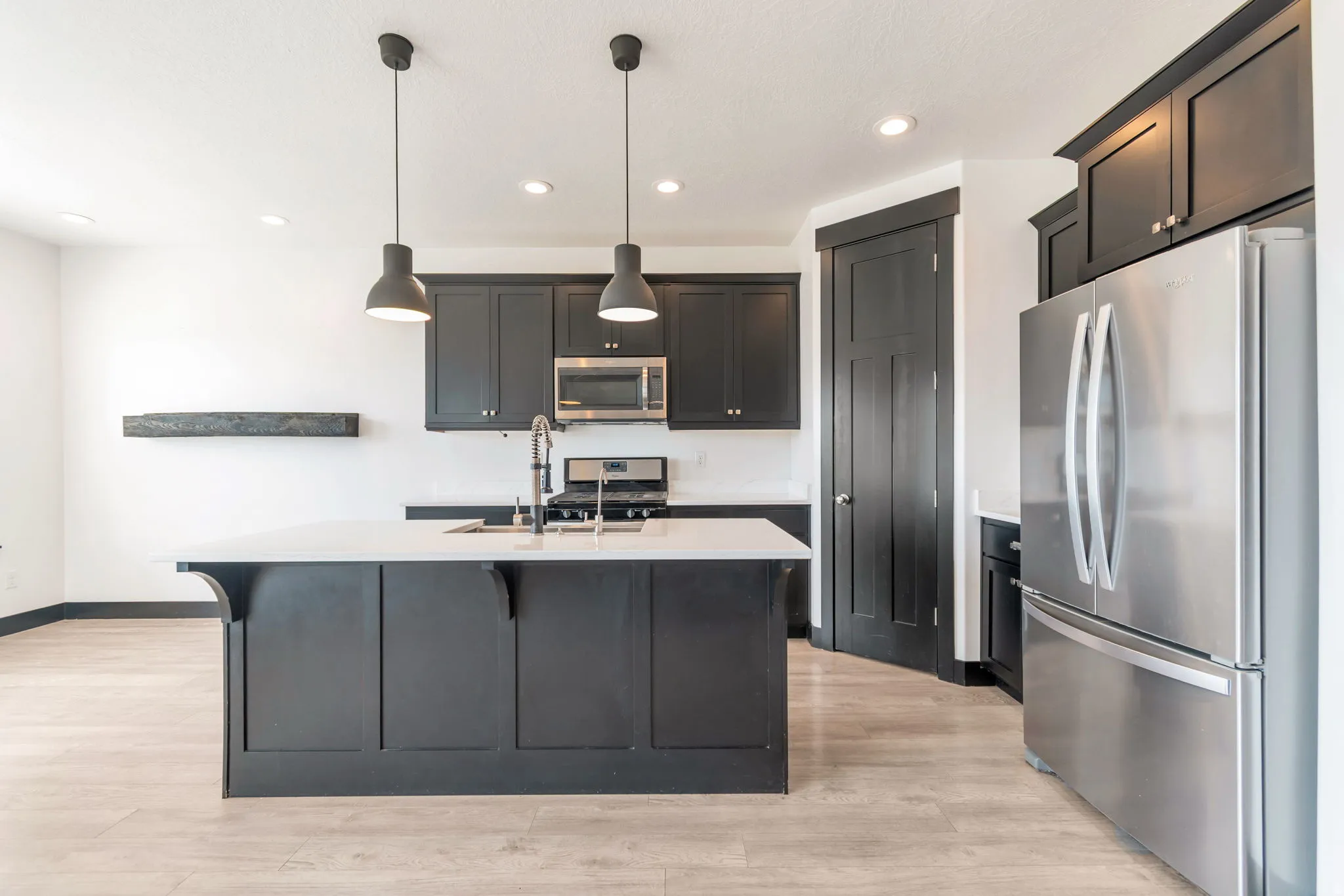 Kitchen featuring a central island with a built-in sink, white countertops, dark cabinetry, stainless steel appliances, and wood-finish flooring