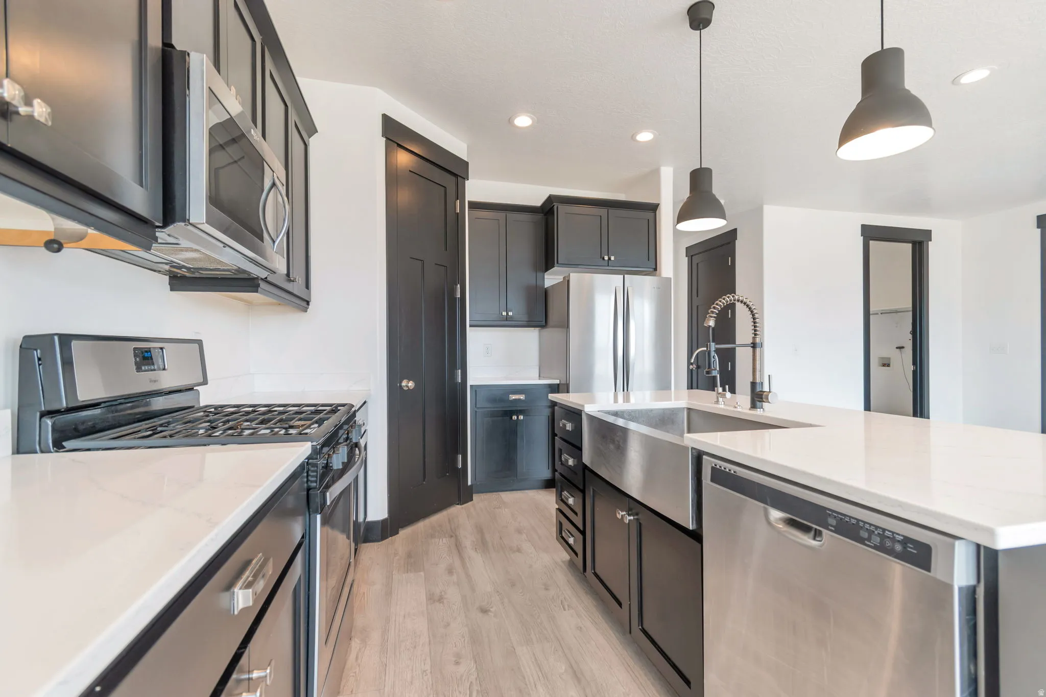 Modern kitchen featuring dark cabinetry, stainless steel appliances, light-toned countertops, and wood-finish flooring