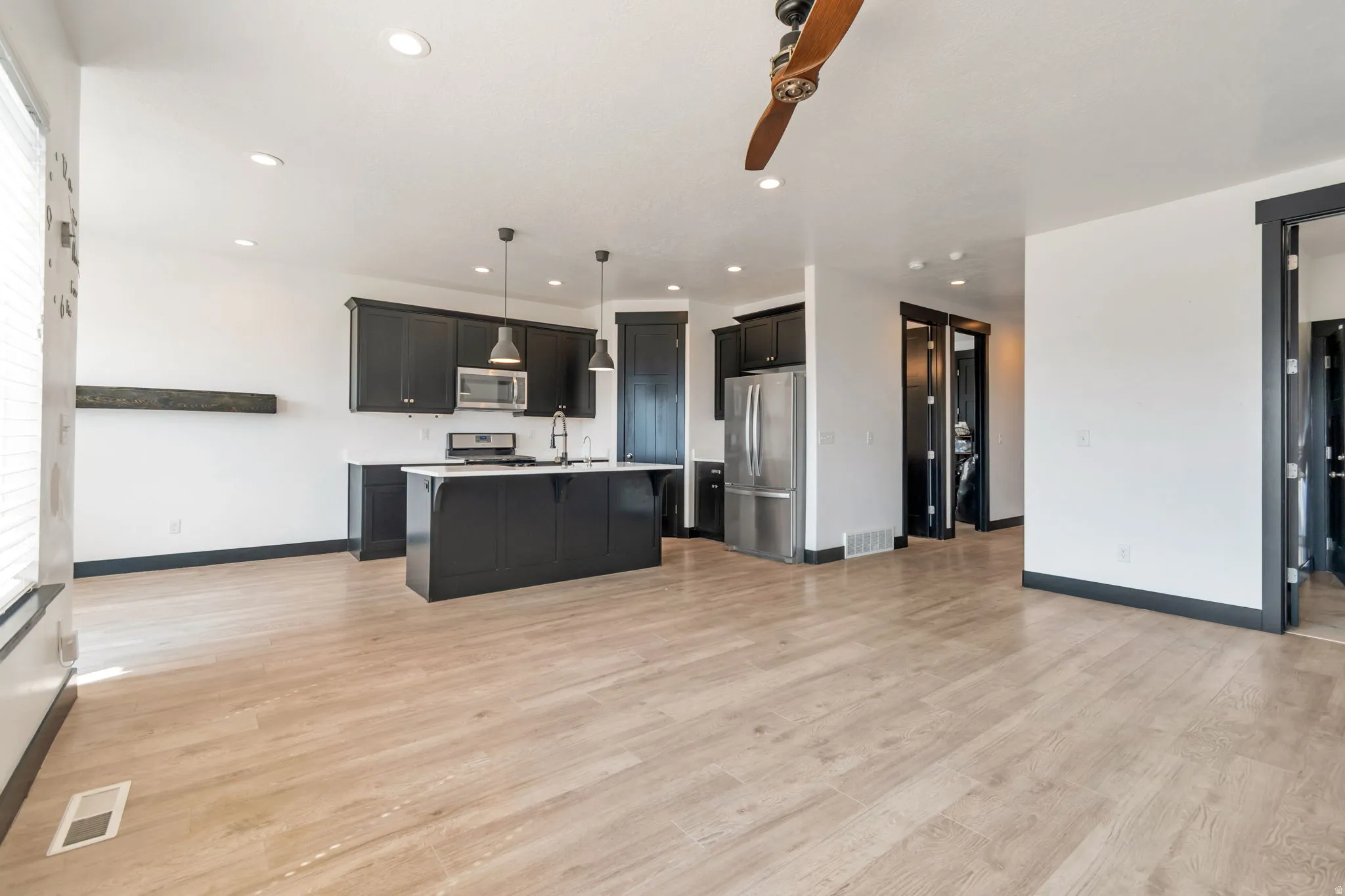 Open-concept kitchen and living area featuring wood-finish flooring, dark cabinetry, and stainless steel appliances