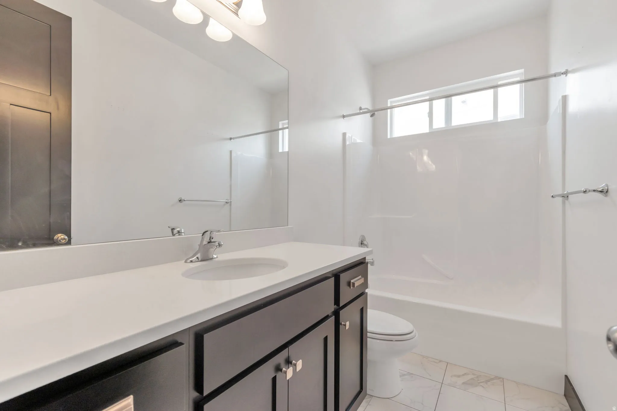 Full bathroom featuring a single vanity with a white countertop and dark wood-finish cabinetry, a built-in tub with shower, and white tile flooring