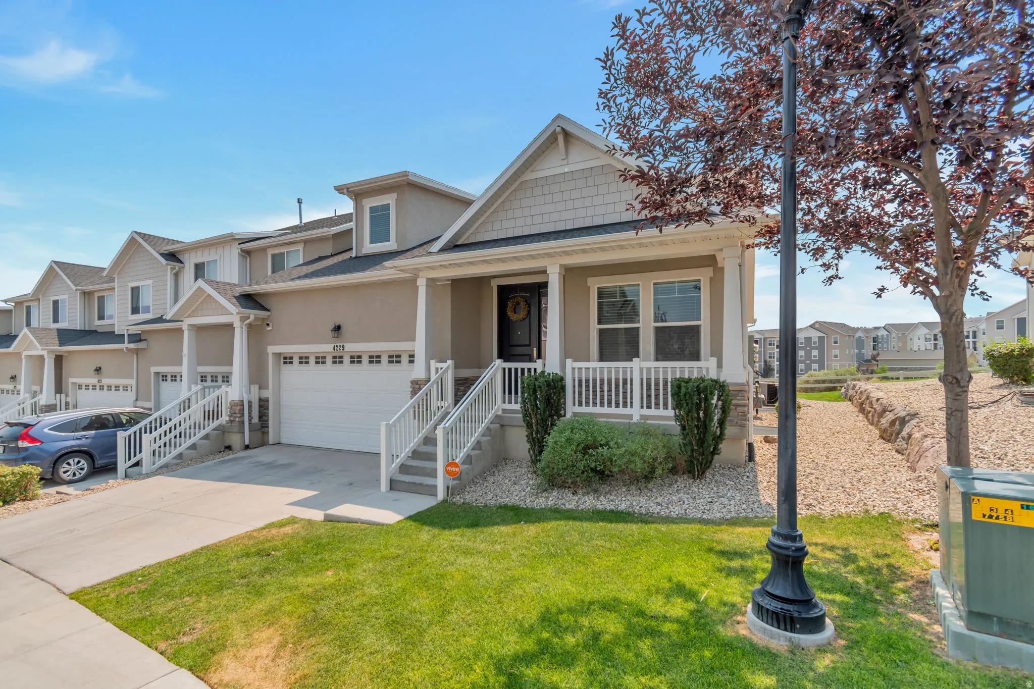 Inviting stucco and siding exterior with stone accents, featuring a covered front porch, an attached garage, and a manicured lawn