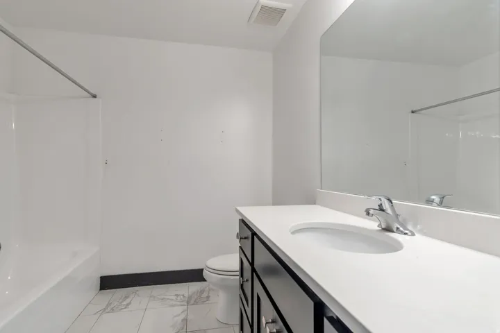 Bathroom featuring a white bathtub, a toilet, a vanity with a white countertop, a basin sink, and a mirrored wall