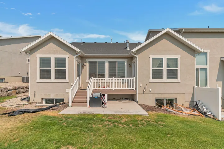 Rear exterior featuring a deck with white railings, a ground-level concrete patio, and a manicured lawn