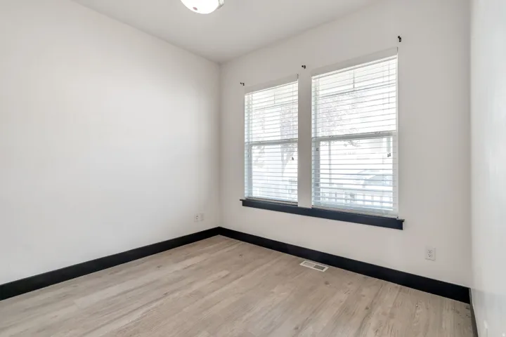Bright room featuring two windows with blinds, a flush mount ceiling light, light wood-finish flooring, and dark baseboards