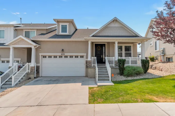 Contemporary residence featuring a covered front porch with white railings, a two-car garage with paneling, and a dormer window