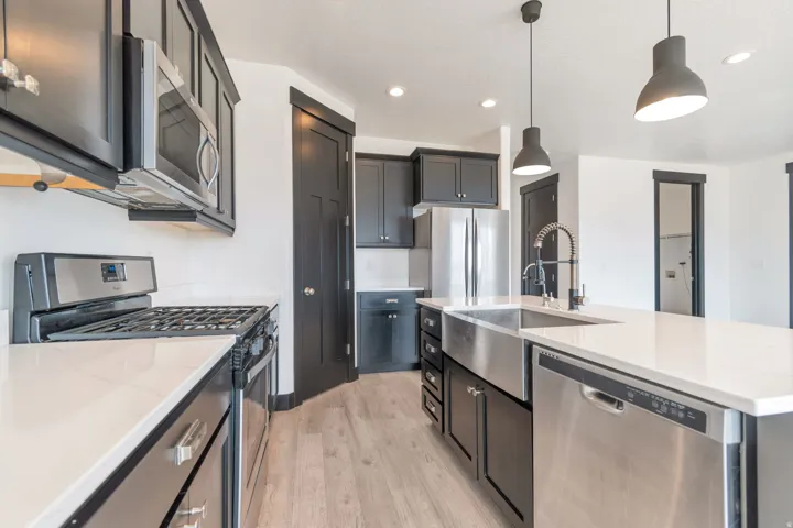 Modern kitchen featuring dark cabinetry, stainless steel appliances, light-toned countertops, and wood-finish flooring