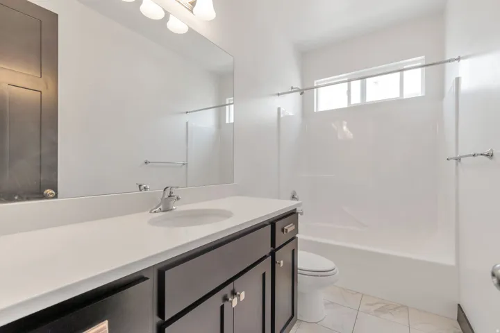 Full bathroom featuring a single vanity with a white countertop and dark wood-finish cabinetry, a built-in tub with shower, and white tile flooring