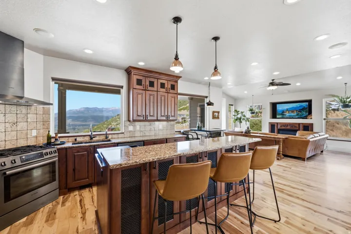 Open-concept kitchen and living area featuring wood-finish flooring, recessed lighting, and a large central island with a stone-finish countertop