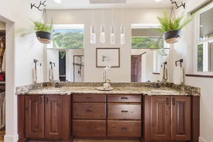 Double vanity with granite countertops, rich wood cabinetry, dual undermount sinks, and a multi-light pendant fixture
