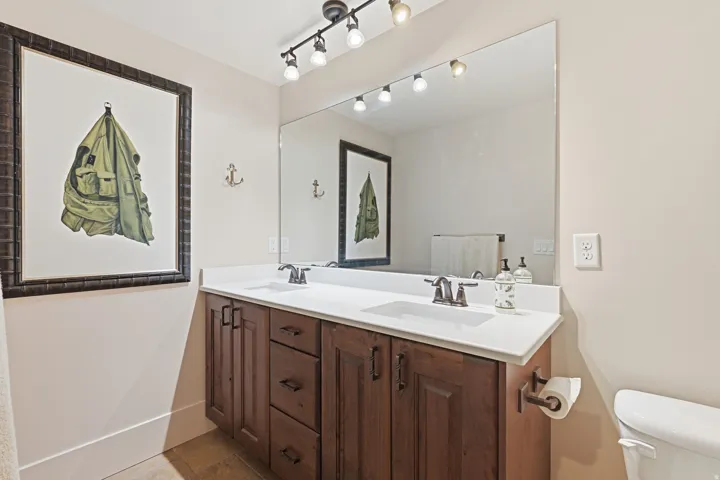Dual sink vanity with dark wood cabinetry, white countertop, and brushed bronze fixtures