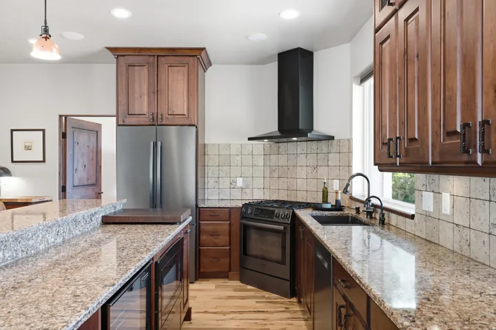 Kitchen featuring granite countertops, wood-finish flooring, stainless steel appliances, a black range hood, and wood cabinetry