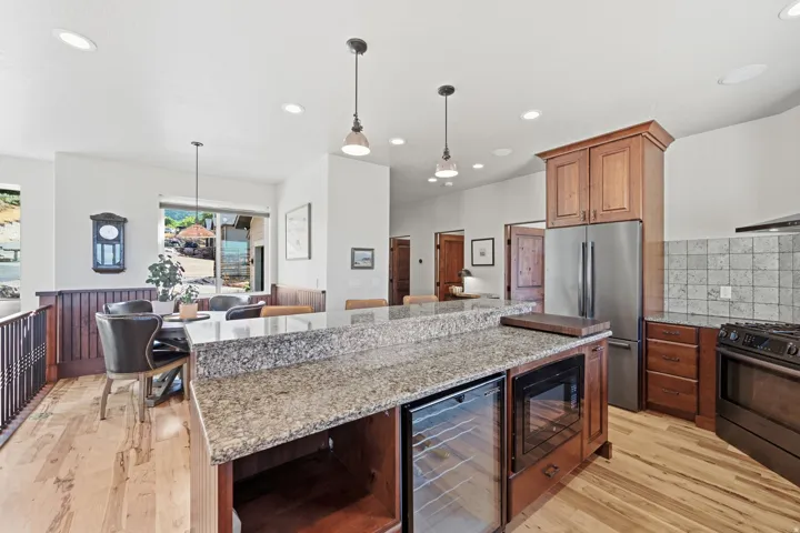 Kitchen featuring wood-finish flooring, a central island with a granite countertop, built-in beverage refrigerator, and microwave, stainless steel refrigerator, and tiled backsplash