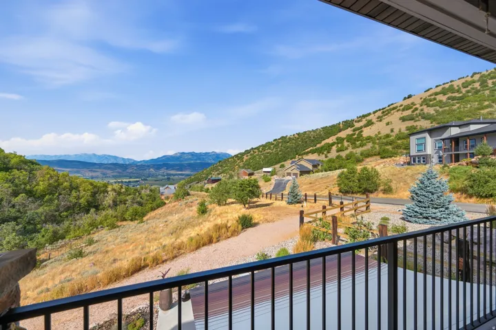 Balcony with black metal railing overlooking a mountainous landscape, distant valley, and surrounding properties