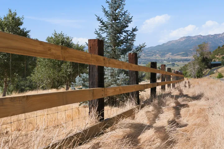 Extensive wood post and rail fencing with wire mesh, surrounded by natural landscaping and distant mountain scenery