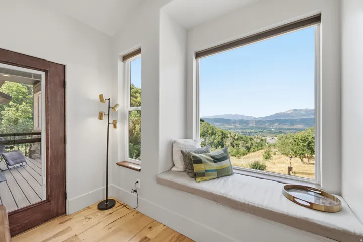 Integrated window seat featuring a large picture window, a secondary vertical window, wood-finish flooring, a wood-framed glass door, and a mountainous backdrop