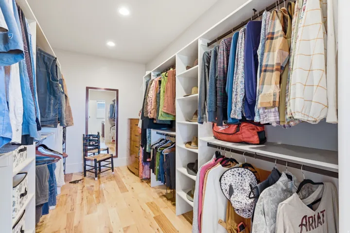 Walk-in closet featuring custom built-in shelving, multiple hanging rods, recessed lighting, and wood-finish flooring