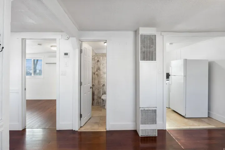 Dark wood-finish flooring extending through an open doorway into a light-filled room with a window