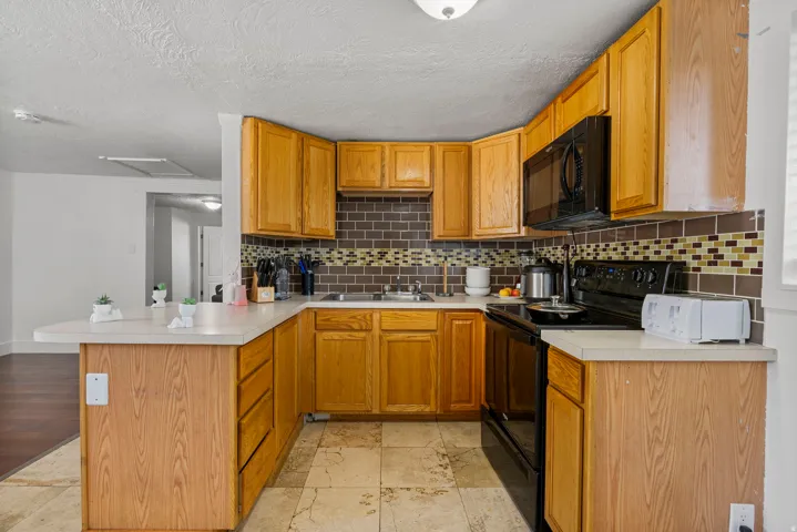 U-shaped kitchen featuring wood-finish cabinetry, light countertops, and a tiled backsplash with mosaic accents