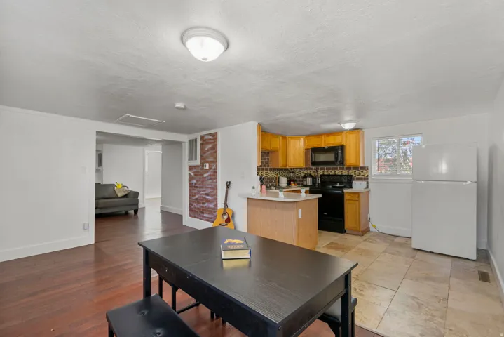 Open-concept living space featuring wood-finish flooring, a kitchen with light wood cabinetry, stone-look tile flooring, black appliances, and a window for natural light