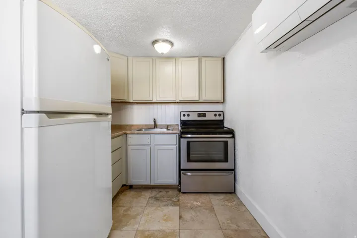 Compact kitchen featuring full-size appliances, including a white refrigerator and stainless steel range