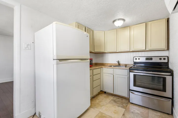 Compact kitchen featuring a white refrigerator, stainless steel range, light-toned cabinetry, light countertop, and tile flooring