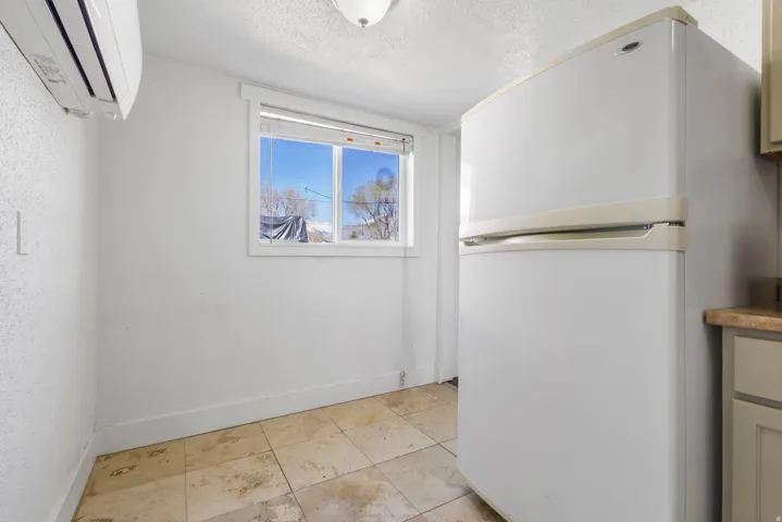 Compact kitchen area featuring tile flooring, a window with horizontal blinds, and a wall-mounted mini-split HVAC unit