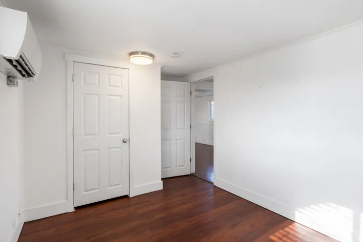 Interior room featuring wood-finish flooring, white walls, and a mini-split air conditioning unit