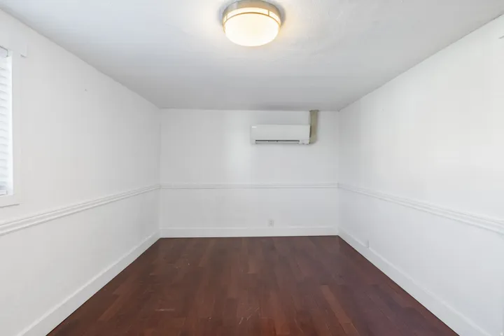 Room featuring rich wood-finish flooring, crisp white walls with chair rail molding, and a window with blinds