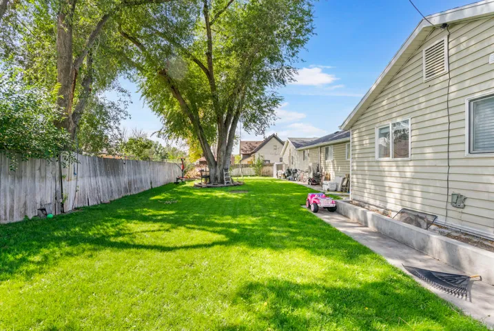 Expansive backyard featuring a manicured lawn, mature shade trees, and a perimeter privacy fence