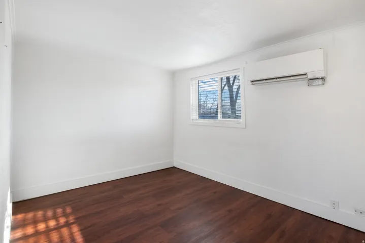 Room featuring wood-finish flooring, white walls, and a window with blinds