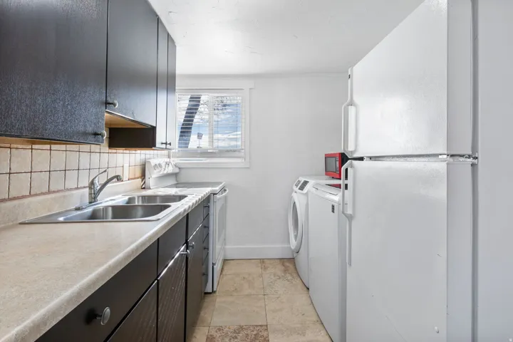 Kitchenette featuring dark cabinetry, a double basin stainless steel sink, and light-toned countertops