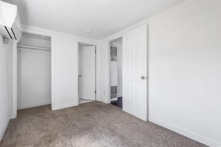 Carpeted room with white walls, a built-in closet with hanging rod, and a wall-mounted air conditioning unit