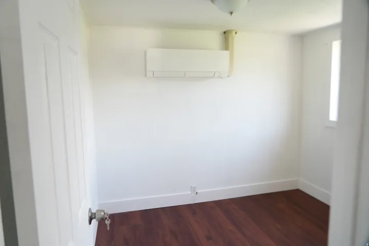 Room featuring wood-finish flooring, white walls, and a wall-mounted mini-split HVAC unit