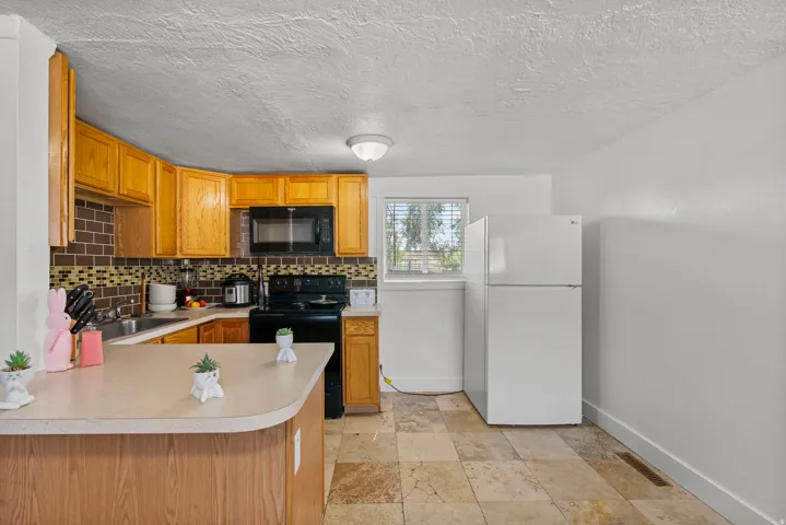 Kitchen featuring wood cabinetry, a built-in microwave, an electric range, a double-basin sink, and a tiled backsplash