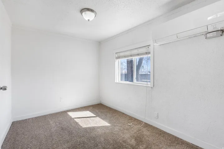 Light-filled room featuring neutral-toned carpeting, white textured walls, and a window with blinds
