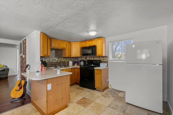 Spacious kitchen featuring warm wood cabinetry, a central island with breakfast bar seating, black electric range and microwave, mosaic tile backsplash, ceramic tile flooring, and ample counter workspace
