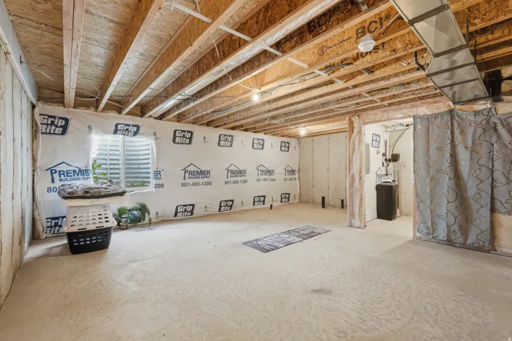 Unfinished basement space featuring exposed wooden ceiling joists, a visible window, and concrete flooring